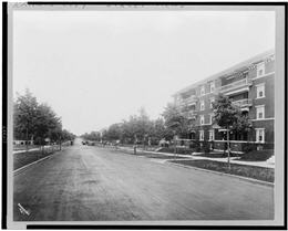 Tree lined residential street with four story building in foreground. Suburban scene.