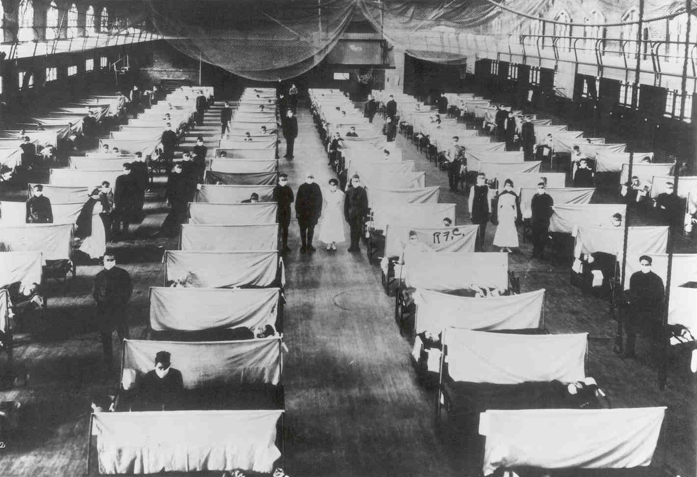 A row of tented beds in a gymnasium.  Doctors and nurses stand by the beds.