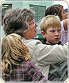 Photograph of a woman and several children signing a large banner.