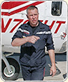 Photograph of a man in dark uniform pointing and standing in front of a helicopter.