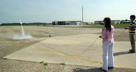 A woman standing on a runway launches a model rocket