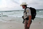 A man wearing a USFWS uniform looks perplexed as he looks out onto a beach