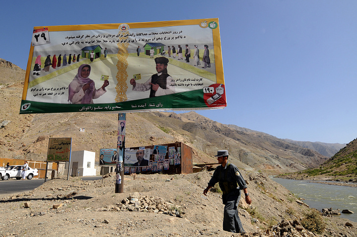 A policeman walks under a billboard featuring a voter education poster in the rugged mountains of the Panjshir Valley.  Nervous residents prepare to elect a president on Aug. 20 after a surge in Taliban attacks as the government lashed out at the media, threatening to expel those who report violence on polling day.  