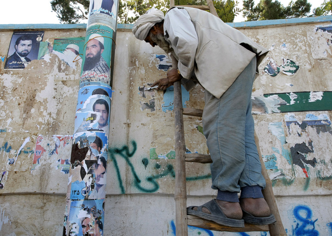 An employee of the Herat municipality removes electoral posters from a wall in Herat, Afghanistan.   