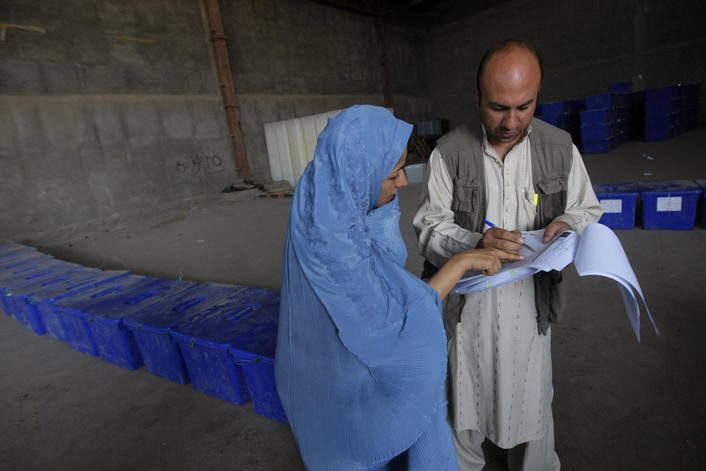 An election official, right, speaks with an employee from the Independent Election Comission (IEC) as she waits for election kits for her village polling station at a government building in Enjil village.  