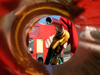 Photo is from the viewpoint of inside a gas tank looking out and shows a person's hand holding a gas pump nozzle and approaching the tank with it.