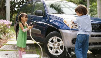 Photo of two kids washing the car as the little girl sprays water on the little boy