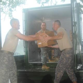 Photo: Sergeant Tate Hudson (left) of Pearl, Miss., passes food to Sgt. 1st Class Jon Mason of Newton, Miss., while Sgt. Tony Ryals of Pelahatchie waits during distribution efforts at the Lyman Senior Citizen Center on August 29. The Soldiers are members of Battery C, 1st Battalion, 204th Air Defense Artillery based in Morton, Miss. They were transporting food provided by the American Red Cross to shelters near Hurley, Miss. (Photo by Staff Sgt. Scott Tynes, 102d MPAD).