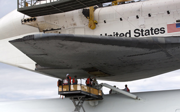 Technicians watch as space shuttle Endeavour is lowered onto the Shuttle Carrier Aircraft, or SCA, at the Shuttle Landing Facility at NASA's Kennedy Space Center in Florida. The SCA, a modified 747 jetliner, will fly Endeavour to Los Angeles where it will be placed on public display.
