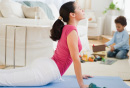 Photo of a woman doing yoga pose while child plays with toys in the background