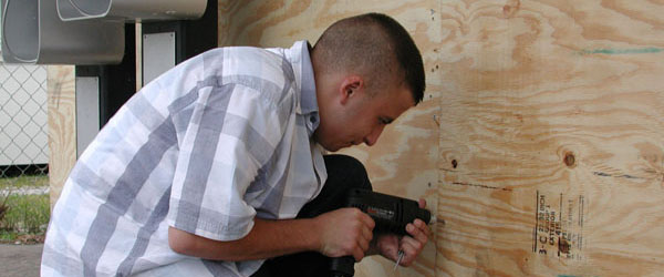 A man nailing plywood over the windows of his home.