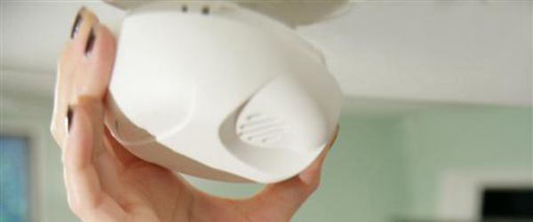 A woman checking a smoke detector. 