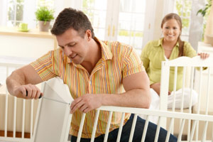 man assembling a crib while a pregant woman watches