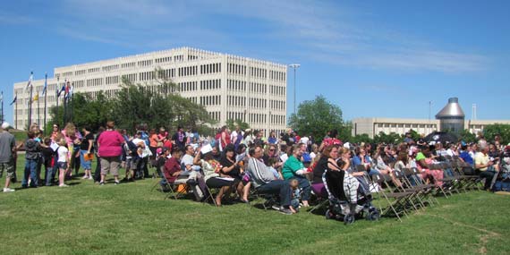 A crowd of people sit outside in rows of chairs at the Oklahoma Systems of Care Community Picnic