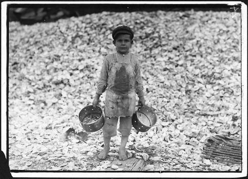 Image description: A five-year-old child laborer named Manuel stands before a mountain of oyster shells in Biloxi, Mississippi in 1912. This image was part of a series of 5,000 photographs taken by Lewis Hine for the National Child Labor Committee. They were used by the Department of Commerce and Labor&#8217;s Children&#8217;s Bureau in both its investigations of child labor issues and advocacy for federal legislation to limit workplace abuses against children.
Hines took pictures of children working as harvesters in agricultural field work; pickers in seafood, vegetable, and fruit canneries; workers in cotton mills and glass, furniture, and cigar factories; as &#8220;breaker boys&#8221; in coal mines; and more.
Image courtesy of the National Archives and Records Administration.