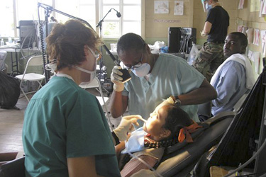 Dental hygienists LCDR Vickie Owens (right) and CDR Sandra Ferguson (left) treat a child at Groves Elementary School in Guyana.