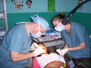 Left to right: LT Charles Brucklier, USPHS dental hygienist, is applying a dental sealant to a young El Salvadoran girl while SSGT April Paulson, dental assistant with the United States Air Force assists. The photo was taken at Unidad de Salud Acajutla, El Salvador.
