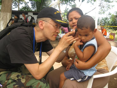 CDR Izune Hwang, a family-practice physician, performs an ear exam with an otoscope to determine if a suspected ear infection is due to fever, ear pain, or hearing loss.