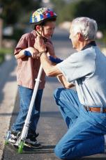 Photograph of a boy with a scooter and a man fastening the boy's helmet