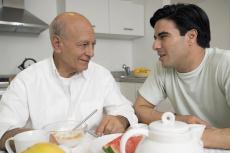 Photograph of an older man and a younger man talking at the breakfast table