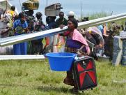 A woman carries a travel bag, a washing basin and a rolled corrugated sheet.