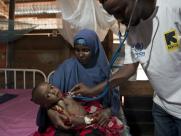 A member of the IRC medical team examines a child in his mother's arms