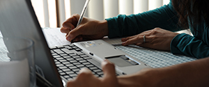 Hands writing notes from a laptop computer screen