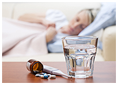 A woman is sick in bed. Water and medicine are in the foreground.