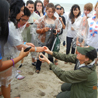 An NPS ranger kneeling on the beach as she holds up a turtle egg for a group of students to see.