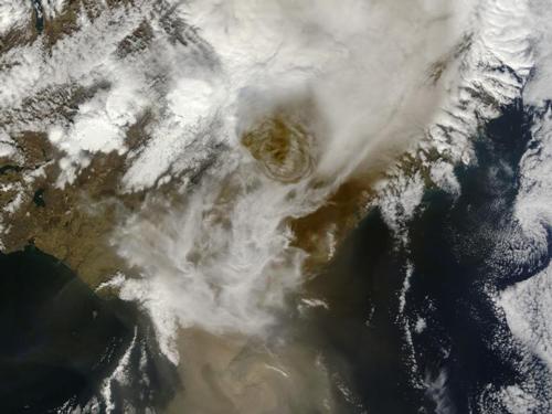From NASA:

On May 21, 2011, Iceland’s Grimsvotn Volcano erupted, sending an ash plume 12 miles (20 kilometers) high and closing Keflavik Airport, Iceland’s largest. Ash fell on much of Iceland, with some areas pitch black at midday on the 22nd. This eruption is not expected to disrupt air travel as much as that of Eyjafjallajokull in 2010 because the Grimsvotn ash particles are larger and settling out of the atmosphere more quickly.
This natural-color satellite image, acquired by the Moderate Resolution Imaging Spectroradiometer (MODIS) aboard the Terra satellite, shows the towering ash plume at 1:00 p.m. local time. Beneath the ash plume, clouds cover much of the scene. Lingering snow is visible beneath the clouds to the northeast (upper left). Brown ash covers a portion of the Vatnajokull Glacier near the Atlantic coast (lower right).
