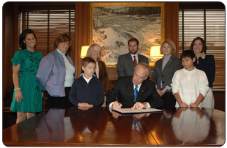 Secretary of the Interior Dirk Kempthorne signs an order extending the authorization of Take Pride in America within the Department of the Interior through the year 2010. Standing, from left in top row, are Take Pride in America Director Katie Loovis; Volunteers Barbara Brown, Jane Collins, and Scott Wilson;  Ms. Davis, a teacher from Hyattsville Elementary School, Hyattsville, Md.; and Interior Deputy Secretary Lynn Scarlett.  In bottom row, from left, are Hyattsville Elementary School student Billy Kennedy; Secretary Kempthorne; and student Jose Cruz. 