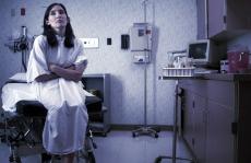 Photograph of a female patient in a hospital gown sitting in an exam room