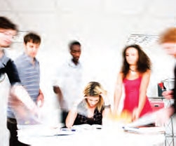 A group of students stand around one who looks distressed as she concentrates on her schoolwork.