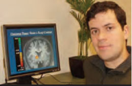 This is a photograph of Dr. Mauricio R. Delgado, with his computer screen displaying a functional magnetic resonance image of the brain.