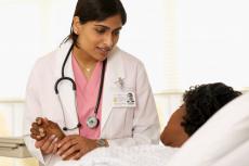 Photograph of a female doctor comforting female patient in a hospital bed