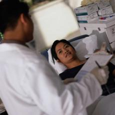 Photograph of a male healthcare professional talking to a woman in a hospital bed