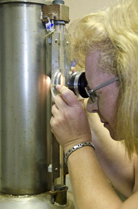 PML technician Sherry Sheckels uses a flashlight and magnification loupe to take exact water-level measurements on a stainless steel container.