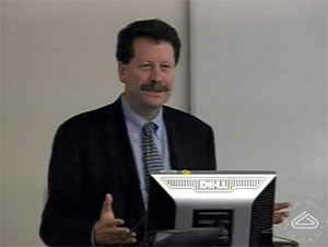 Man with a moustache speaks at a podium
