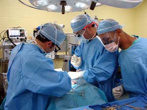 Three surgeons in scrubs around a patient covered in surgical drapes