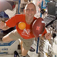 A football and an orange floating in front of Anderson on the space station