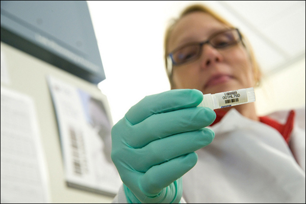 A female lab technician holds a vial containing a hepatitis sample.