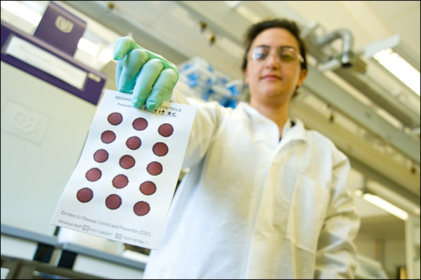 A CDC scientist holds a test strip of blood samples taken for newborn screenings.