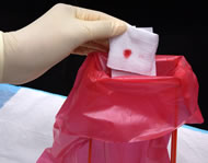 gloved hand holding blood-stained gauze pad over disposal bag