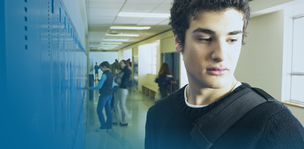 Image of teenage boy standing in school hallway with other teens in background