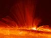 Vivid orange streamers of super-hot, electrically charged gas (plasma) arc from the surface of the Sun, revealing the structure of the solar magnetic field rising vertically from a sunspot.
