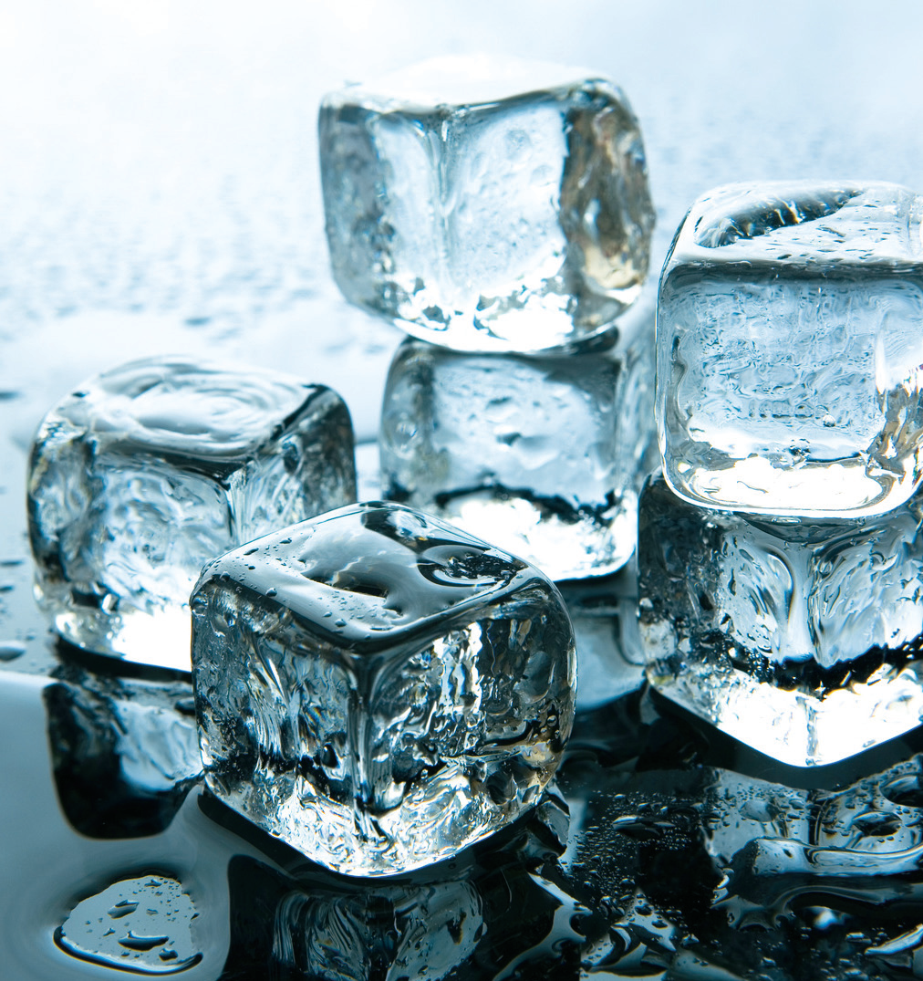 Image of small ice cubes, some stacked on top of each other, melting on a black surface.