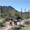 Thumbnail image of a group of men and women walking on a dirt trial near tall cacti and desert brush.