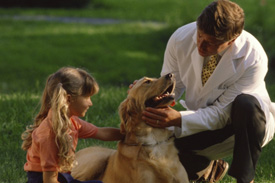 man in white lab coat with a girl looking at a dog