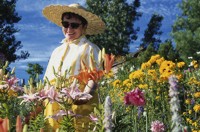 Photo of a woman in a garden wearing a hat, sunglasses, and a long-sleeved shirt