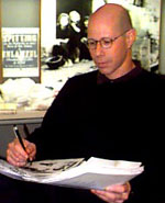 Half-length photograph of Michael Sappol wearing glasses looking downat papers he is holding with his left hand and a pen in his right.